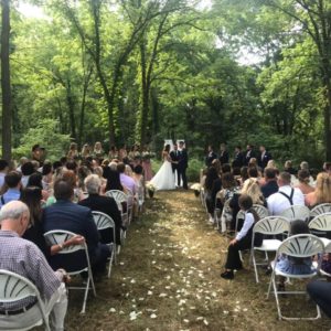 Ann Arbor garden wedding with bride & groom exchanging vows as wedding guests dressed in formal wear are seated 